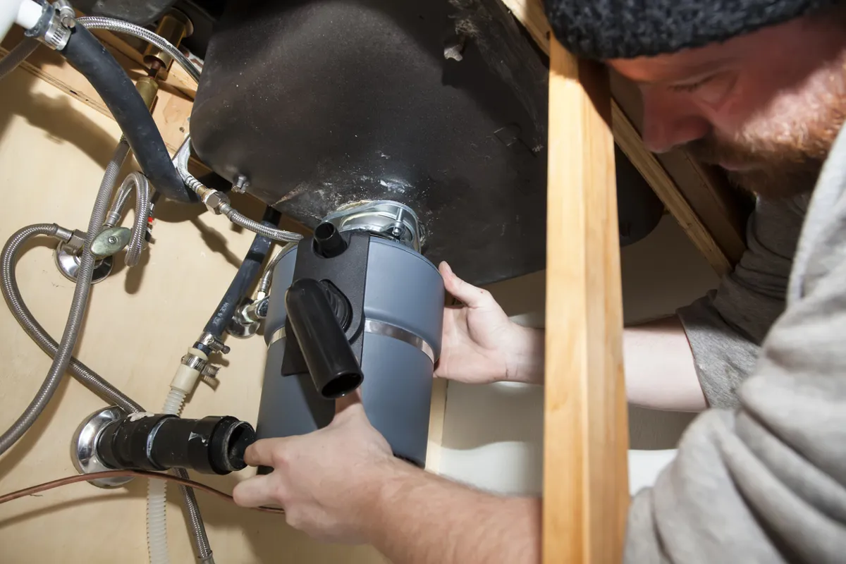 Will Fix It Plumber installing a garbage disposal in a home.