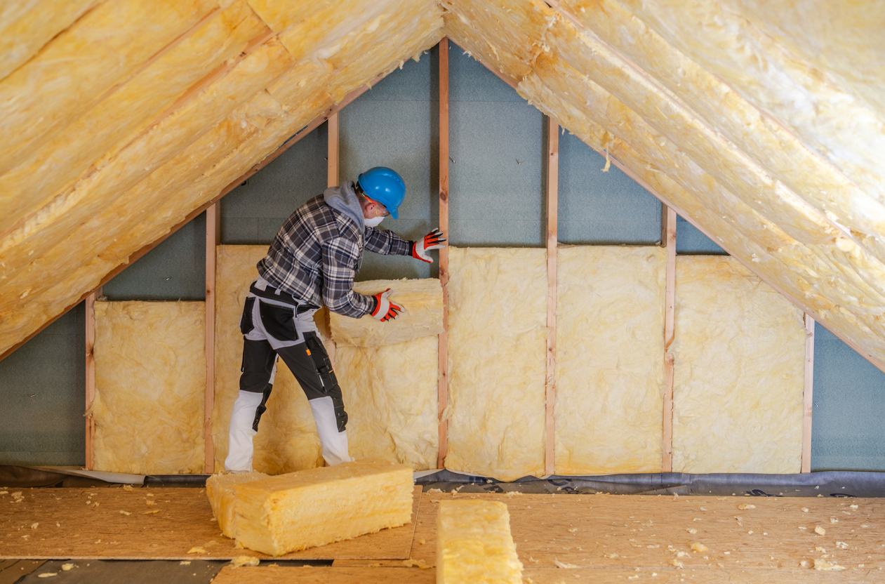 A contractor installs fiberglass insulation between attic wall studs to improve home energy efficiency.